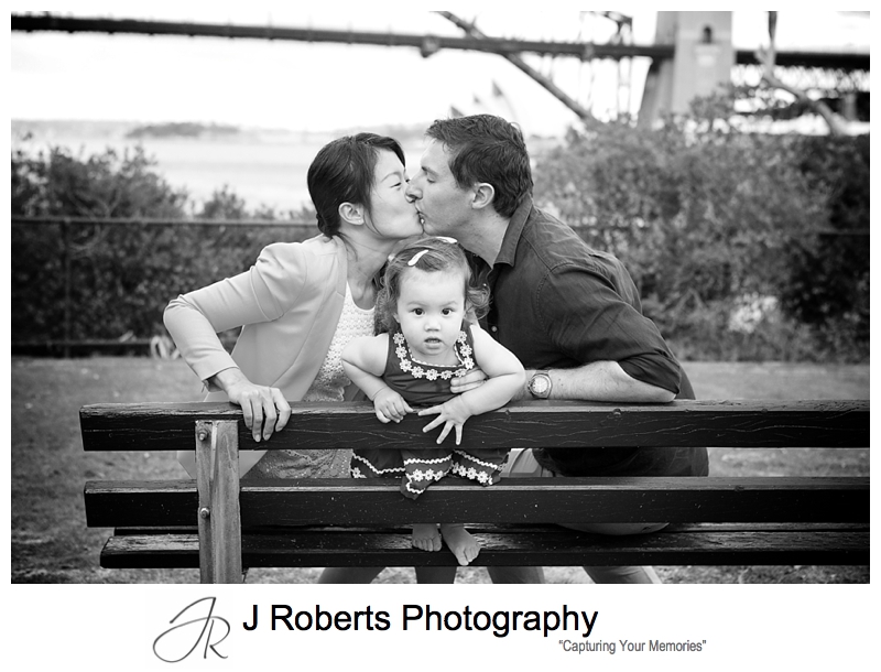 Family portrait of little girls with parents kissing behind her - sydney family portrait photographer